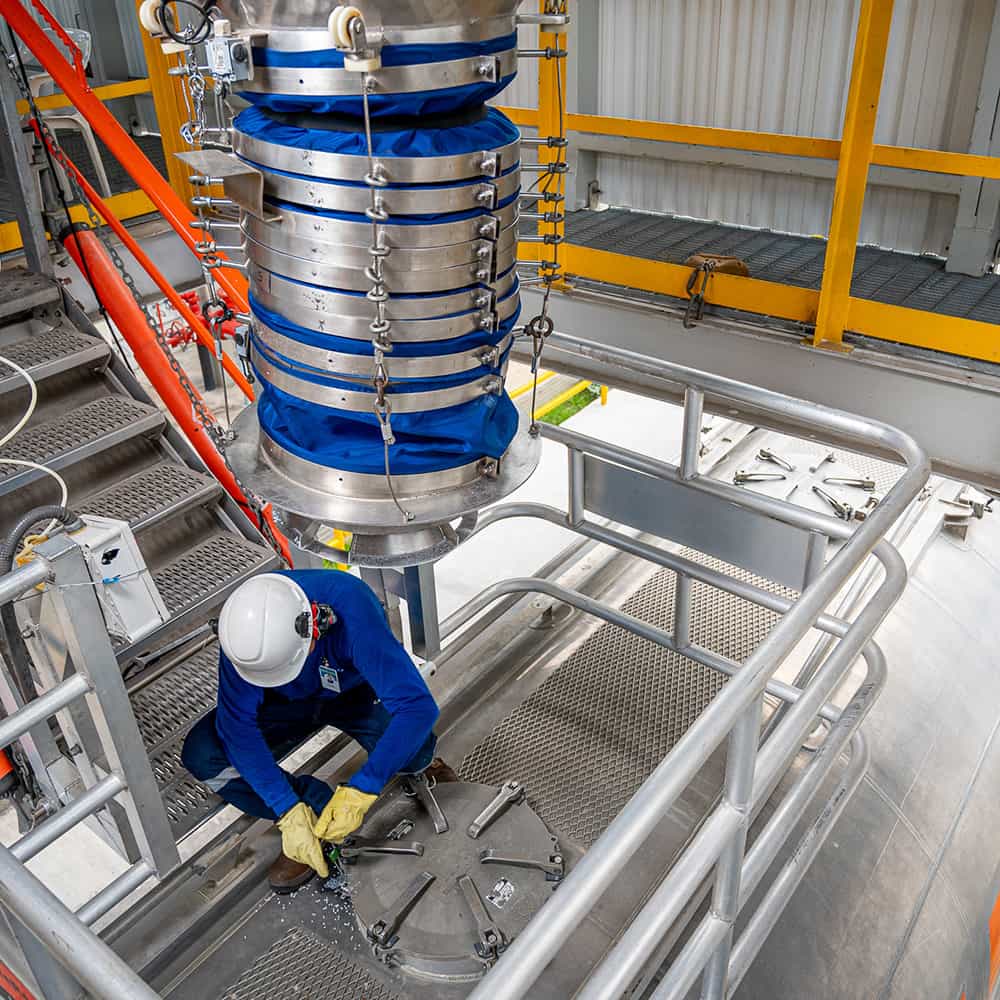Worker kneels on the floor to adjust manufacturing equipment