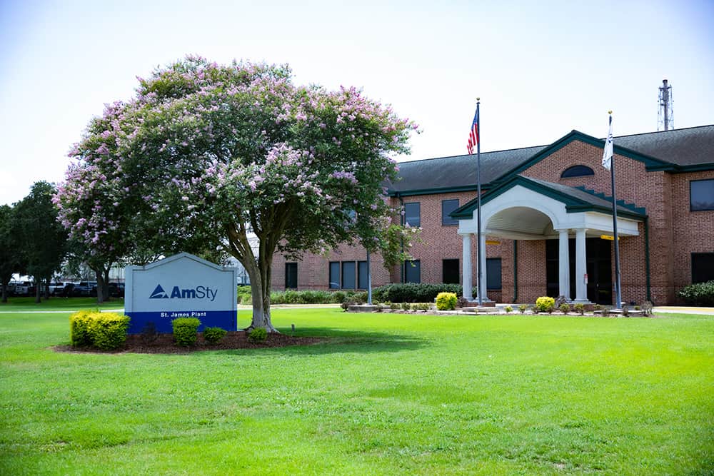 An outside view of an office with an AmSty company sign, American flag on a pole and a tree blooming