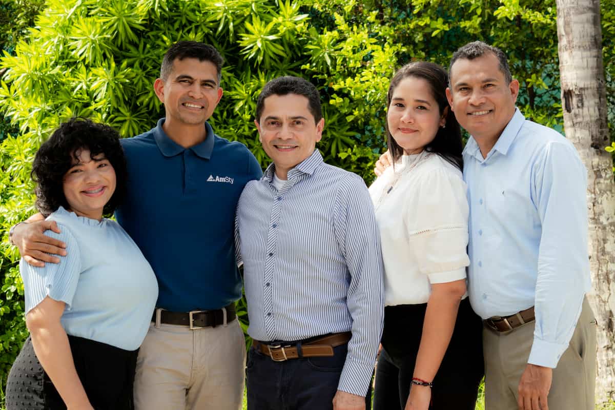 A group of employees in AmSty apparel pose in front of green foliage
