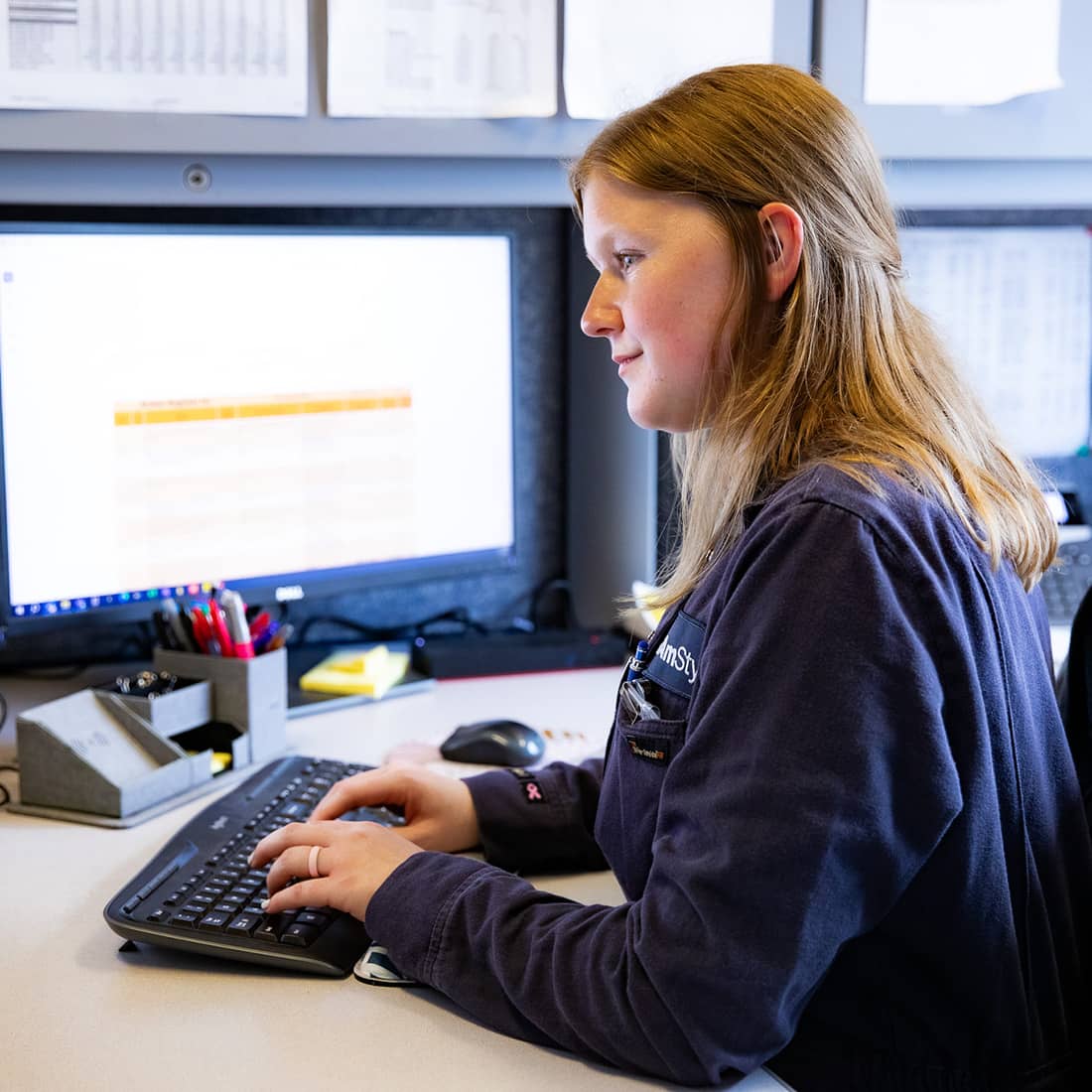 A young, female AmSty employee with long blonde hair typing on a keyboard at an office desk in front of a computer monitor